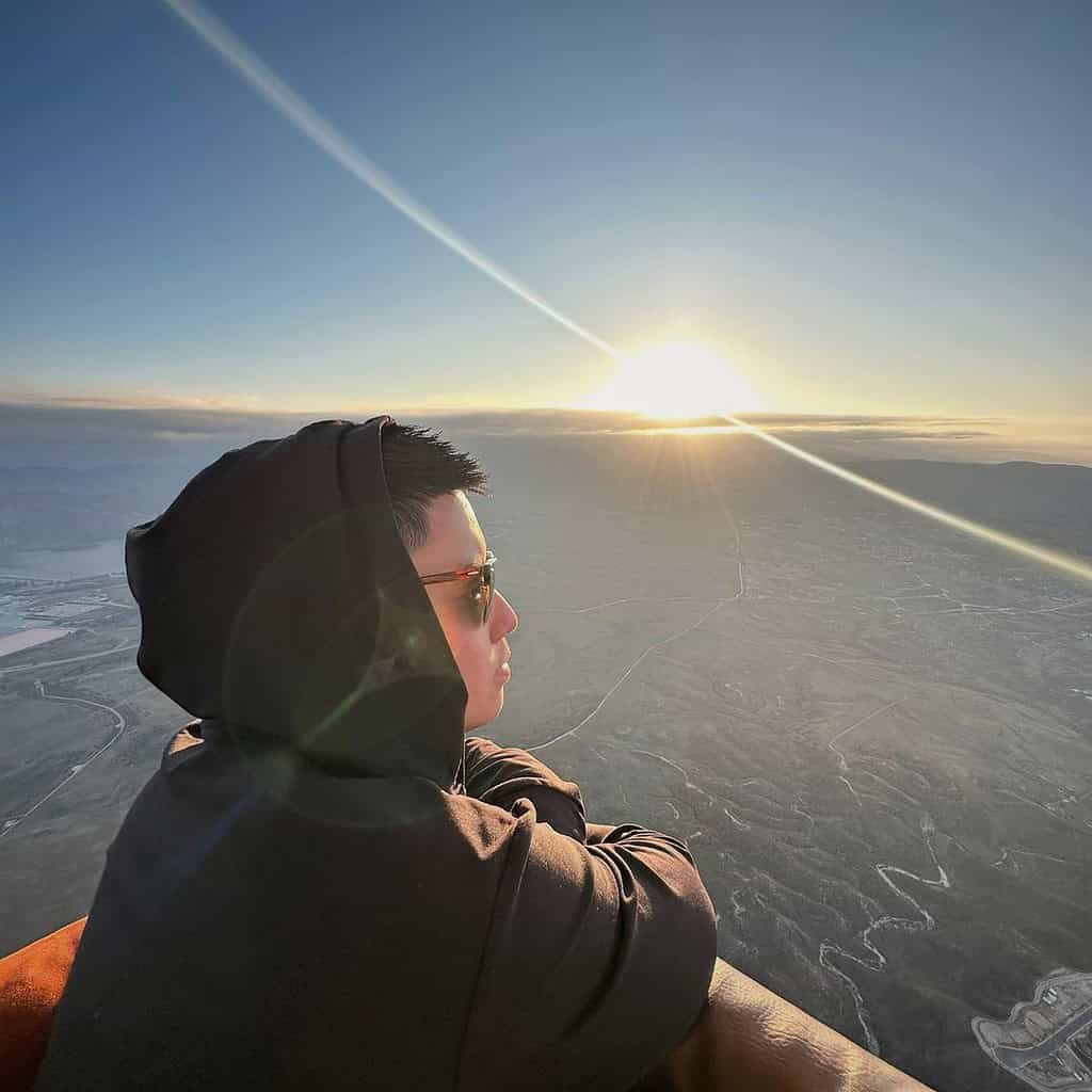 Person enjoying sunrise view from a hot air balloon.